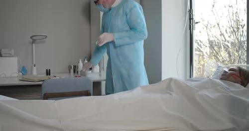 Man in Face Mask and Protective Gloves Taking Care of Covid-19 Positive Patient in Hospital Ward