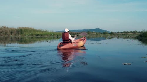 Back young adult woman paddling kayaking canoe on a lake on summer day