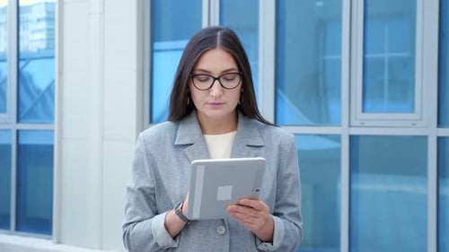 Woman in a Formal Suit and Glasses Walks and Looks at the Tablet on the Street Slow Motion