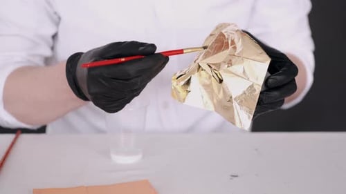 Nahaufnahme von Händen in Handschuhen mit Pinsel und Maltopf
