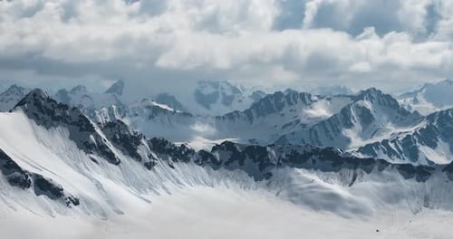 Air Flight Through Mountain Clouds Over Beautiful Snowcapped Peaks of Mountains and Glaciers