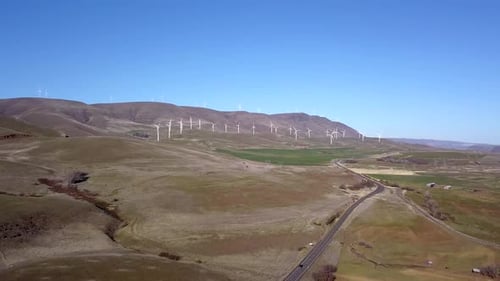 Aerial drone flying toward a renewable energy wind turbine farm.