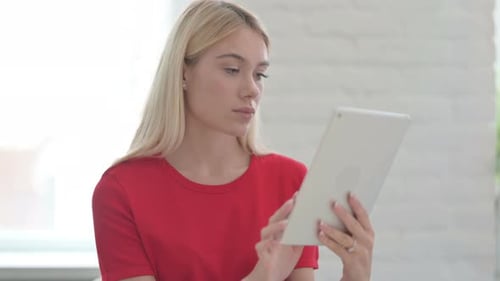 Verärgerte junge blonde Frau reagiert auf Verlust auf Tablet