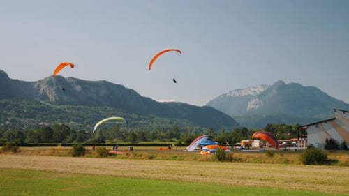 Orange paragliders going on landing at landing strip in Alps mountains