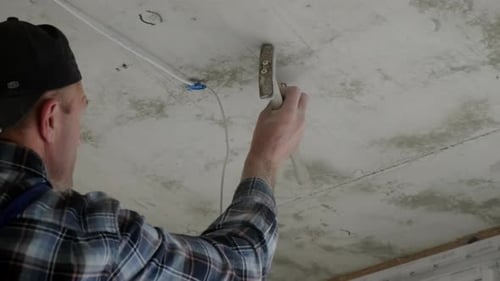 Man Securing Wiring to Ceiling with Hammer