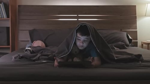 Garçon asiatique regardant dessin animé sur tablette avant le coucher