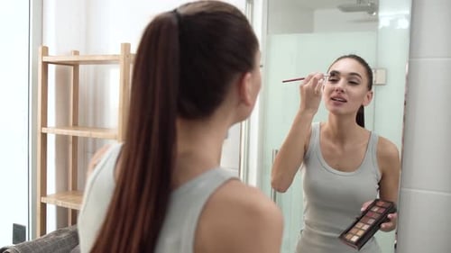 Woman Applying Makeup in Front of Mirror