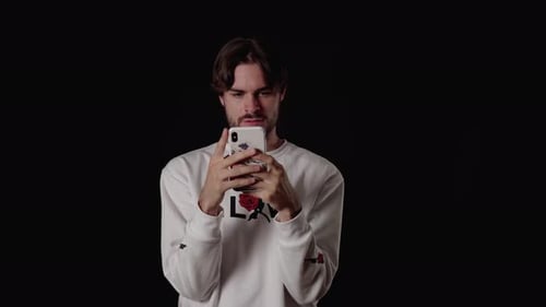 Trendy Young Man using and considered typing on phone, wide, black background
