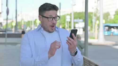 Man Celebrates Good News on Smartphone in City