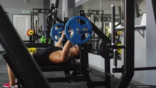 Male Bodybuilder Trains in Gym Lying on Bench and Lifting Barbell Side View