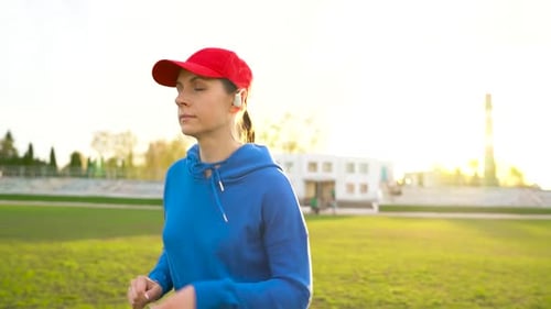 Woman with Wireless Headphones Runs Through the Stadium at Sunset