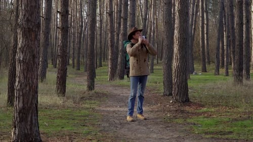 Ein Mann mit Hut und Rucksack macht Fotos im Wald