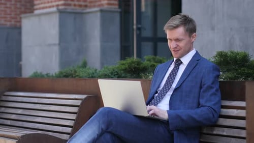 Excited Businessman Using Laptop Outdoors