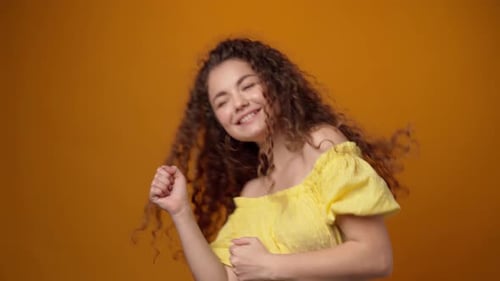 Woman Smiles and Dances Against Orange Background