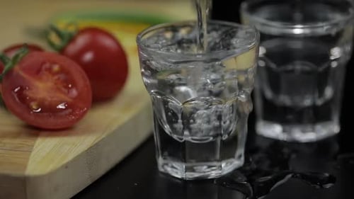 Pour Alcohol Drink Vodka From a Bottle in Shot Glass. Surface with Snacks