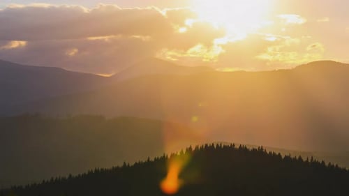 Beautiful Evening Panoramic Landscape with Bright Setting Sun Over Distant Mountain Peaks at Sunset