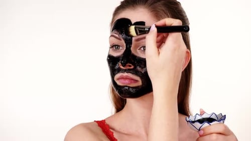 Woman Applies Black Cosmetic Mask to Face