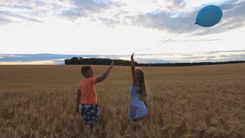 Little Girl and Boy Standing in Wheat Field and Releasing From Hands Balloon Into the Sky. Cute