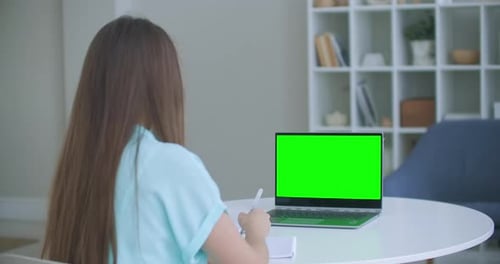 Girl Taking Notes in Notepad From Laptop Computer Green Mockup Screen. Girl Learning Online on