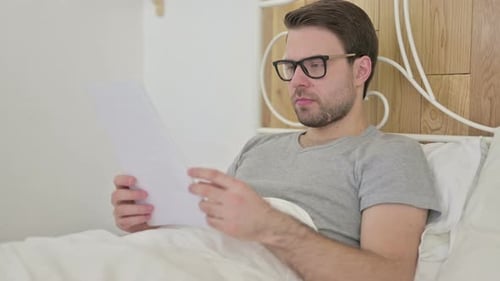 Man Reading Papers in Bed