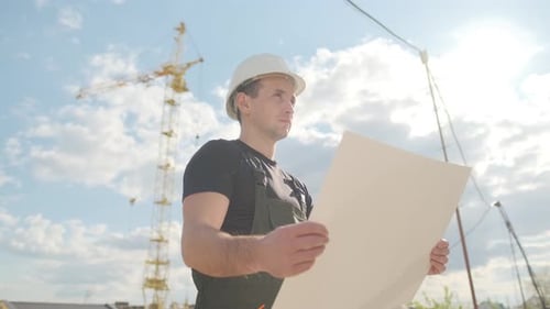 Construction Worker Examines Building Blueprint at Site