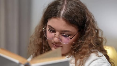 Young Adult Woman Smiling While Reading Book Indoors