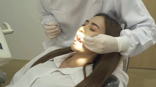 A dentist checking up Asian woman patient's teeth by using dental mouth mirror