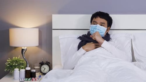 Unwell Adult Coughing in Bed Wearing Mask