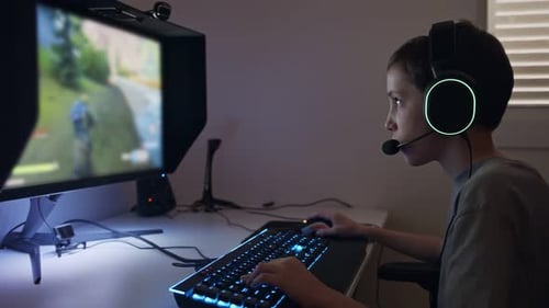 Kleiner Junge sitzt vor einem Computer und spielt ein Spiel mit einem Headset