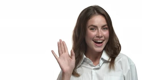 Closeup of Attractive Brunette Woman Saying Hi and Waving Hand Smiling at Camera Standing Over White