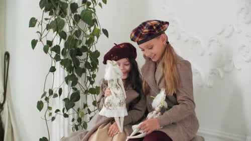 Entzückende stilvolle Mädchen in Mänteln und Baretten posieren mit eleganten Vintage-Puppen