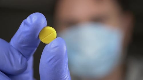 Gloved Hand Holding a Yellow Pill Close Up