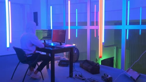 Lieu de travail d'un hacker : hacker travaillant dans une pièce avec des néons colorés
