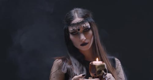 Woman Holding Skull Candle in Dark and Smoky Setting