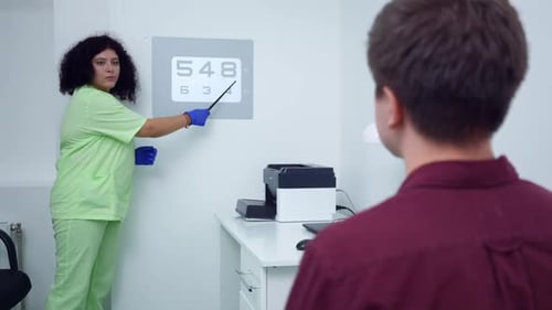 Serious Ophthalmologist Pointing at Numbers Checking Eyesight of Blurred Patient in Medical Clinic