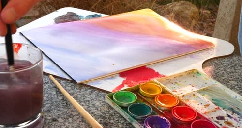 An artist painting a rainbow gradient and mixing colors with watercolor in an outdoor art studio.