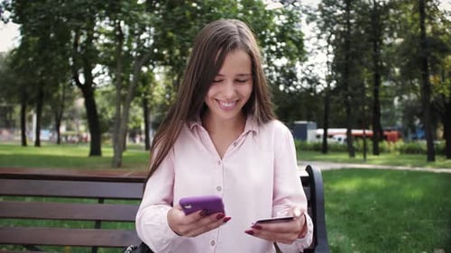 Woman Using Smartphone with Credit Card on Park Bench
