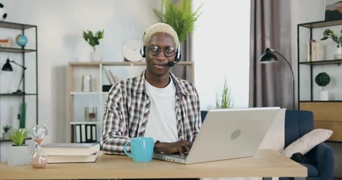 Black-Skinned Gay with Blond Hair in Headset which Sitting in front of Camera in Home office