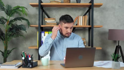 Man Working at Desk Puts Wireless Earbuds In