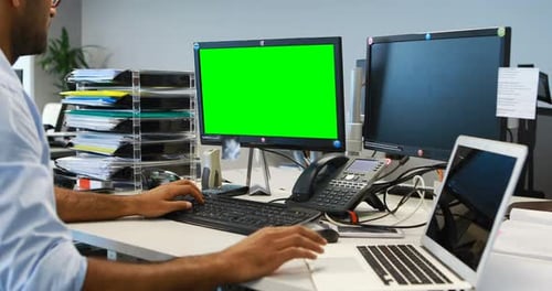 Man Working at Desk with Green Screen Monitor