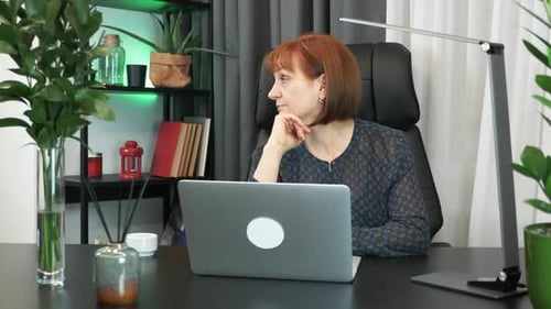 Nachdenkliche ernsthafte Frau sitzt mit Laptop am modernen Schreibtisch und denkt an Problemlösung