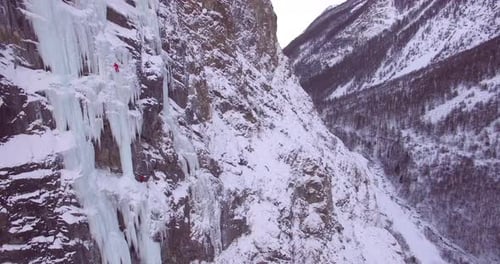 Drohnenaufnahme eines Mannes, der auf einem gefrorenen Wasserfall in den Bergen eisklettert