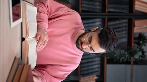 VERTICAL VIDEO POV Clever Man Attentively Reading Paper Book Turning Pages at Desk of Library