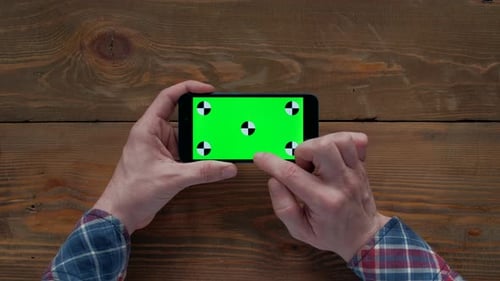 Man Using Smartphone with Green Screen on Wooden Table