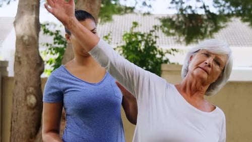 Senior Woman Assisted with Gentle Stretching Exercises Outdoors