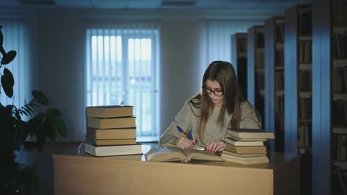 Beautiful Young Girl with Glasses Studying in Library Taking Notes From Books