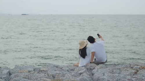 Young Couple Sitting on Beach Taking Photo