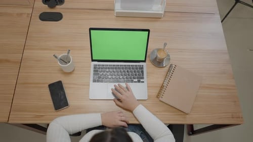 Office Table with Green Screen Laptop Computer and Female Hands Taping or Scrolling on Pad