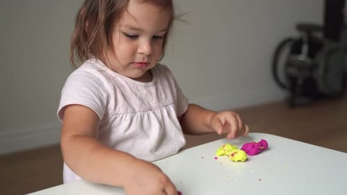 Little Girl Plays with Colorful Modeling Clay at Table