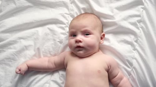 Cute Infant Lying on White Bed Sheet Smiling